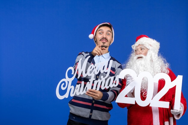 Vorderansicht weihnachtsmann mit jungen männlichen halten und frohen weihnachten schriften auf blauem weihnachtsfeiertag