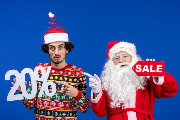 Vorderansicht weihnachtsmann mit jungen männlichen halten und verkaufsschriften auf blauer schneefarbe neujahr weihnachtsfeiertage