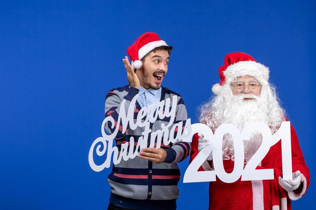 Vorderansicht Weihnachtsmann mit jungen männlichen Holding und Frohe Weihnachten Schriften an blauen Weihnachtsfeiertagen