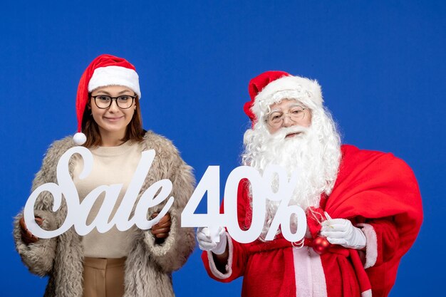 Vorderansicht weihnachtsmann mit junger frau, die verkaufsschriften auf blauer weihnachtsweihnachtsfarbe hält