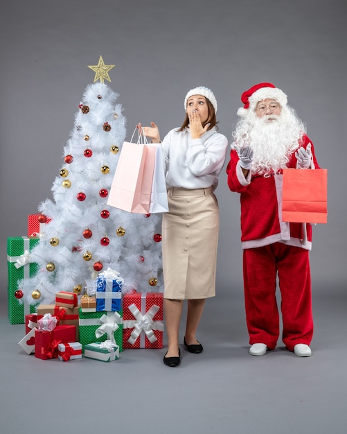 Vorderansicht weihnachtsmann mit junger frau um weihnachtsbaum und präsentiert auf dem grauen hintergrund