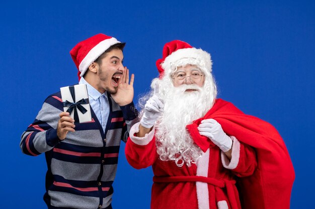 Vorderansicht weihnachtsmann mit junger männlicher tragetasche voller geschenke auf blauem emotionen urlaubsgeschenk weihnachten