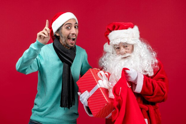 Vorderansicht weihnachtsmann mit männlichem geschenk aus tasche auf roter weihnachtsemotionsfarbe