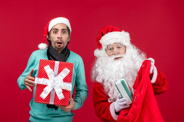 Vorderansicht Weihnachtsmann mit männlichem Herausnehmen von Geschenken aus der Tasche auf rotem Geschenk Weihnachtsgefühl rot