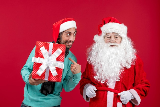 Vorderansicht weihnachtsmann mit männlichen halten feiertagsgeschenk auf roten emotionen roten geschenken weihnachten neues jahr