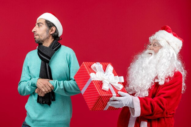 Vorderansicht weihnachtsmann mit männlichen holding urlaubsgeschenk auf rotem schreibtisch rotes geschenk weihnachten emotion neues jahr