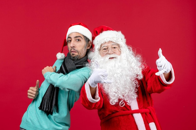 Vorderansicht weihnachtsmann mit männlichen posiert auf den roten anwesenden weihnachten weihnachtsgefühlen