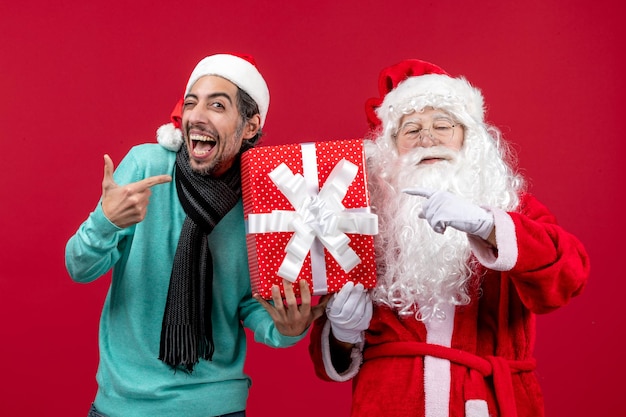 Vorderansicht weihnachtsmann mit mann, der feiertagsgeschenk auf rotem emotion rotem geschenk weihnachten neues jahr hält