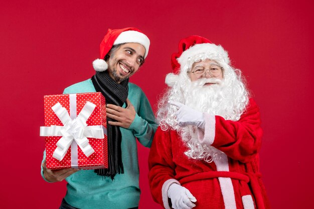 Vorderansicht weihnachtsmann mit mann, der feiertagsgeschenk auf rotem emotion rotem geschenk weihnachten neues jahr hält