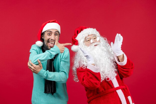 Vorderansicht weihnachtsmann mit mann, der gerade auf rotem weihnachtsfeiertagsgeschenk steht