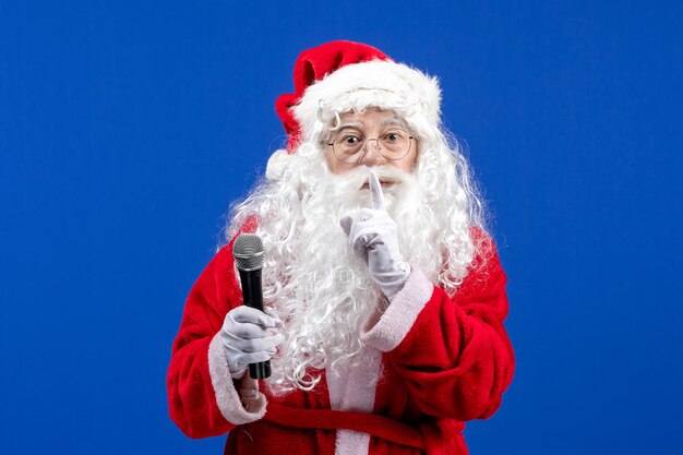 Vorderansicht Weihnachtsmann mit rotem Anzug und weißem Bart, der Mikrofon auf blauem Neujahrsfest hält