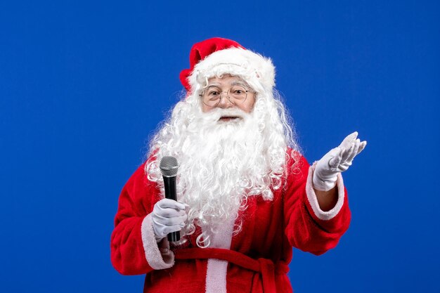 Vorderansicht weihnachtsmann mit rotem anzug und weißem bart, der mikrofon auf der blauen farbe neujahrsfeiertagsweihnachtsemotion hält
