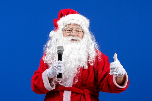 Vorderansicht Weihnachtsmann mit rotem Anzug und weißem Bart mit Mikrofon auf blauem Boden Schneeurlaub Weihnachten Farbe Neujahr