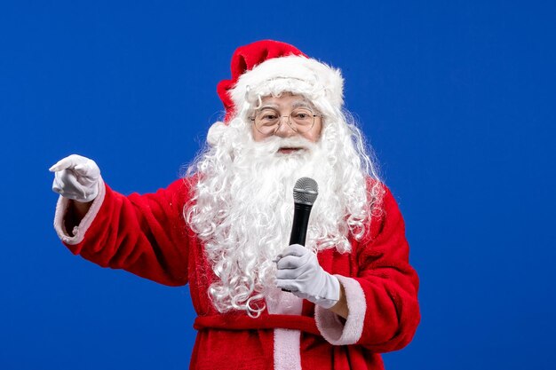 Vorderansicht weihnachtsmann mit rotem anzug und weißem bart mit mikrofon auf blauer weihnachtsfarbe des neuen jahres