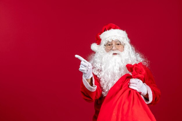 Vorderansicht weihnachtsmann mit roter tasche voller geschenke auf rotem weihnachtsneujahrsfeiertagsgefühl