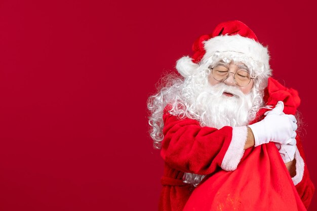 Vorderansicht weihnachtsmann mit roter tüte voller geschenke für kinder auf rotem schreibtisch neues jahr