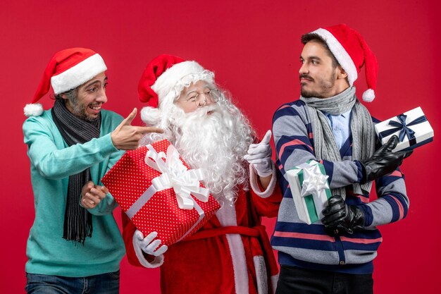 Vorderansicht Weihnachtsmann mit zwei Männern, die Geschenke auf dem roten roten Neujahrsgeschenk Emotion Weihnachten halten