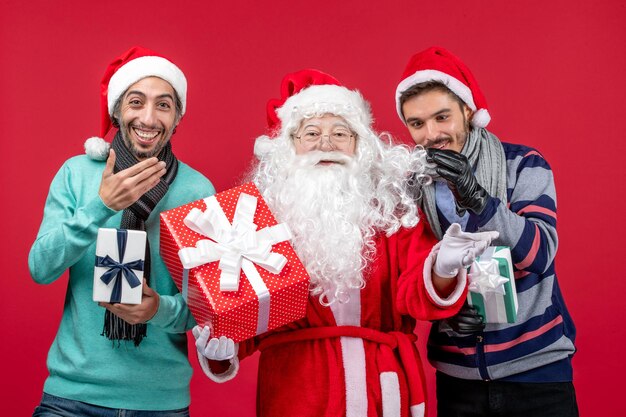 Vorderansicht Weihnachtsmann mit zwei Männern, die Geschenke auf rotem rotem Neujahrsgeschenk Emotion Weihnachten halten