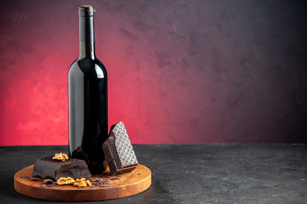 Vorderansicht Weinflasche Walnussstücke dunkle Schokolade auf Holzbrett auf rotem Hintergrund