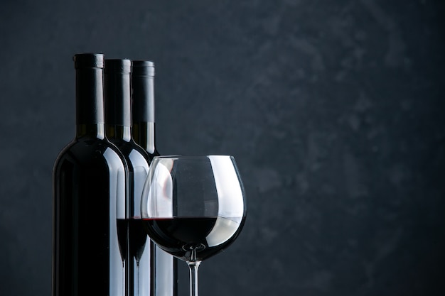 Vorderansicht weinflaschen mit glas wein auf der dunklen oberfläche