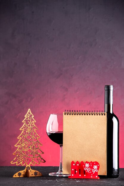 Vorderansicht Weinglas und Flasche Weihnachtsdekoration Notizblock auf rotem Hintergrund