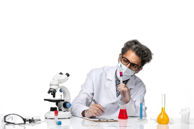 Vorderansicht Wissenschaftler mittleren Alters im weißen medizinischen Anzug, der fertige Injektion hält und Notizen schreibt