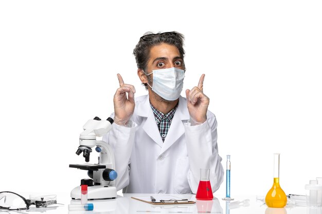 Vorderansicht Wissenschaftler mittleren Alters im weißen medizinischen Anzug, der um Tisch mit Lösungen sitzt