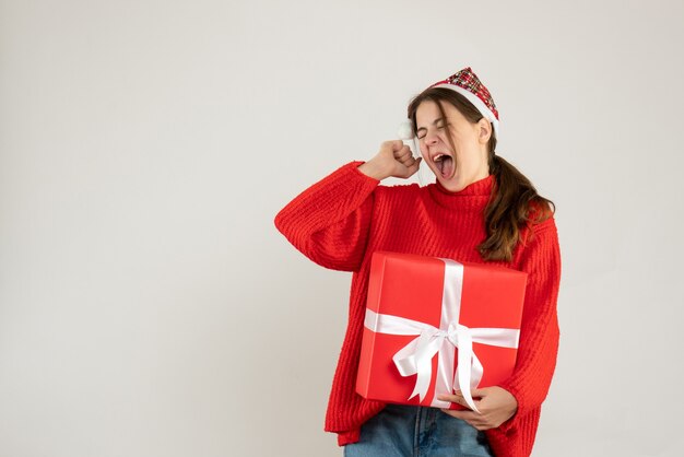 Vorderansicht wütendes süßes Mädchen mit Weihnachtsmütze, die Geschenkschreien hält