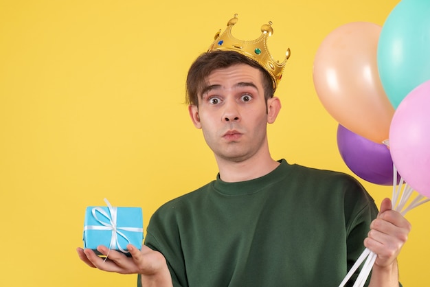Vorderansicht wunderte sich junger Mann mit Krone, die Luftballons auf Gelb hält