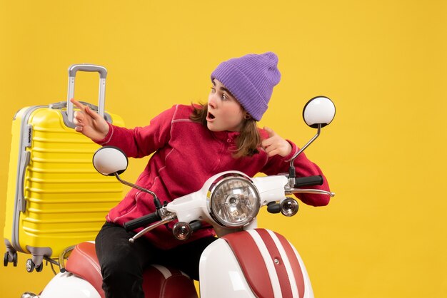 Vorderansicht wunderte sich junges Mädchen auf Moped, das auf etwas zeigte
