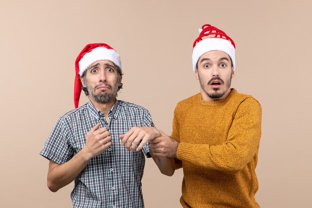 Vorderansicht zwei depressive Kerle mit Weihnachtsmützen auf beigem isoliertem Hintergrund