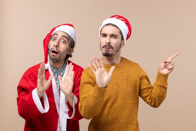 Vorderansicht zwei Freunde mit Weihnachtsmützen überraschend auf beige isoliertem Hintergrund