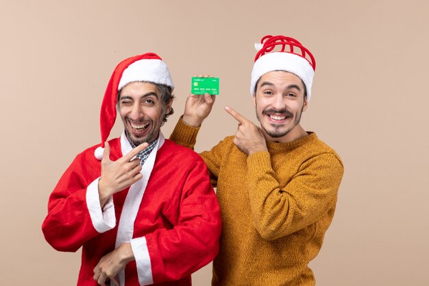 Vorderansicht zwei glückliche Kerle einer mit Santa Mantel und der andere mit Kreditkarte lächelnd auf beige lokalisiertem Hintergrund