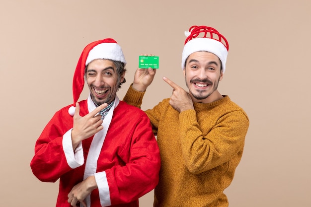 Vorderansicht zwei glückliche Kerle einer mit Santa Mantel und der andere mit Kreditkarte lächelnd auf beige lokalisiertem Hintergrund