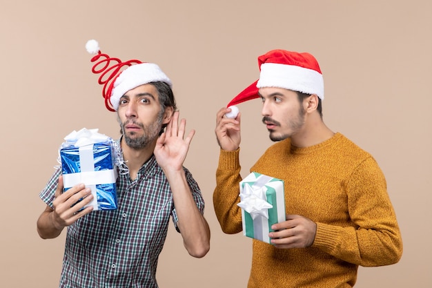 Vorderansicht zwei interessierte jungs, die weihnachtsmützen tragen und geschenke halten