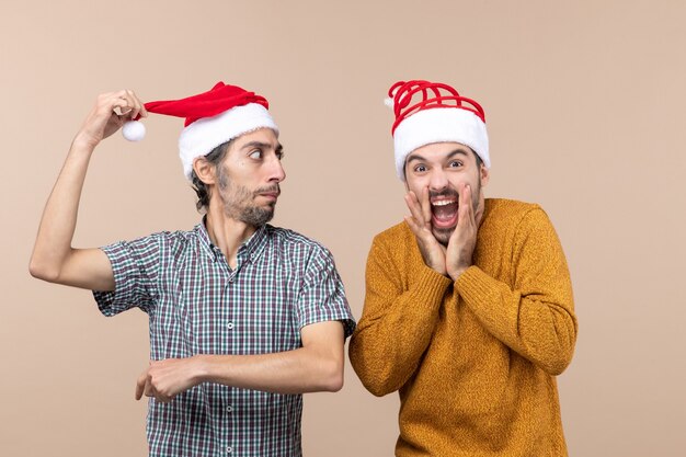 Vorderansicht zwei Kerle, einer, der seine Weihnachtsmütze hält, der andere, der auf beigem isoliertem Hintergrund schreit