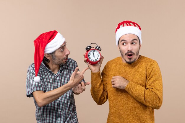 Vorderansicht zwei Männer eine fragende Zeit und die andere zeigt einen Wecker auf beigem isoliertem Hintergrund