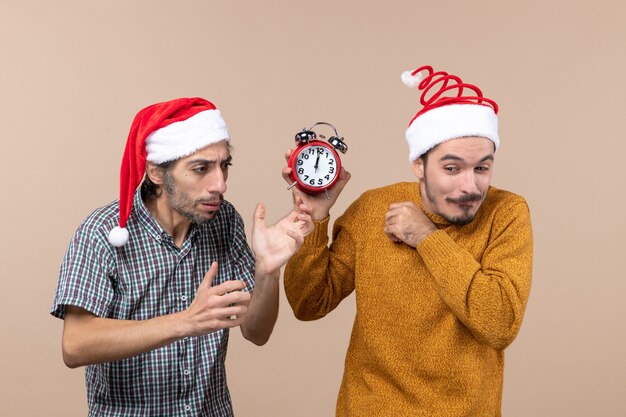 Vorderansicht zwei Männer einer verwirrend und der andere hält einen Wecker auf beigem isoliertem Hintergrund