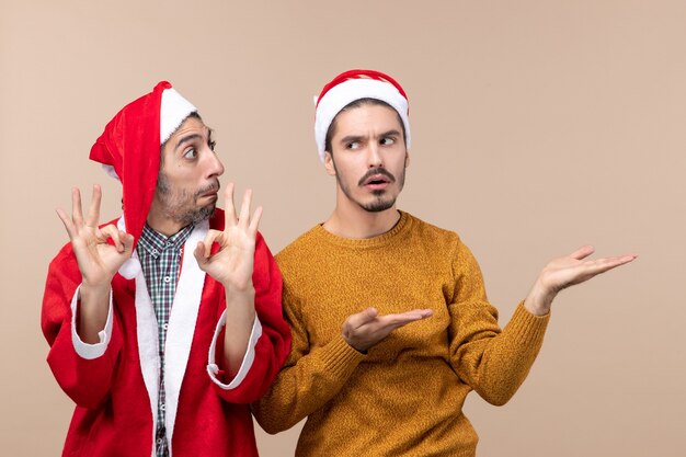 Vorderansicht zwei Männer, von denen einer okay Zeichen macht und der andere etwas auf beigem isoliertem Hintergrund zeigt
