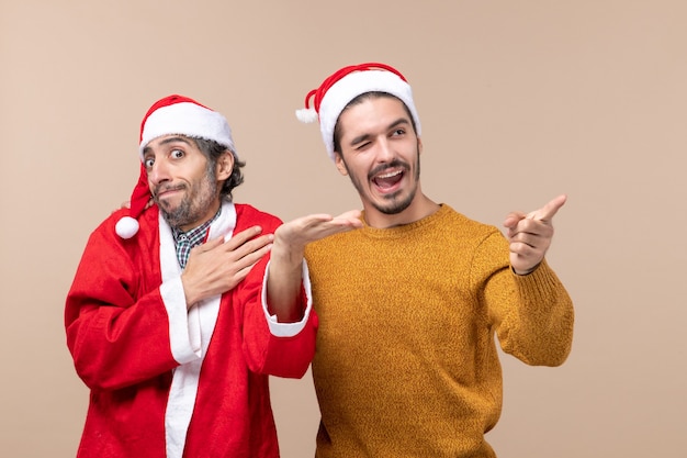 Vorderansicht zwei Weihnachtsmänner mit Weihnachtsmützen, die auf beigem lokalisiertem Hintergrund stehen