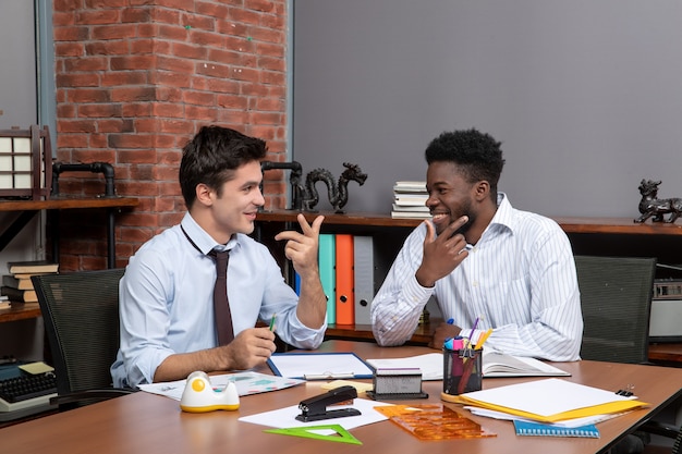 Vorderansicht zwei zufriedene Geschäftsleute, die am Schreibtisch sitzen und im Büro zusammenarbeiten