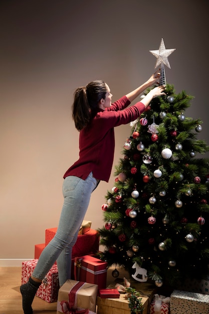 Vorderansichtfrau, die auf Weihnachtsbaum den Stern setzt