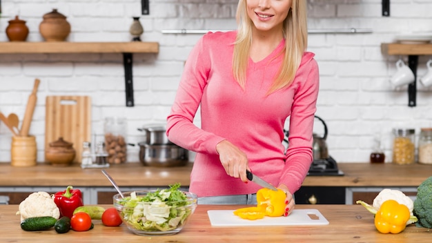 Vorderansichtfrau, die Gemüsepaprika in der Küche schneidet