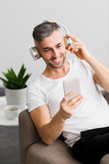 Vorderansichtkerl mit Kopfhörern lächelnd an seinem Telefon