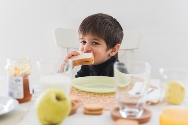 Kostenloses Foto vorderansichtkind, das bei tisch sandwich isst