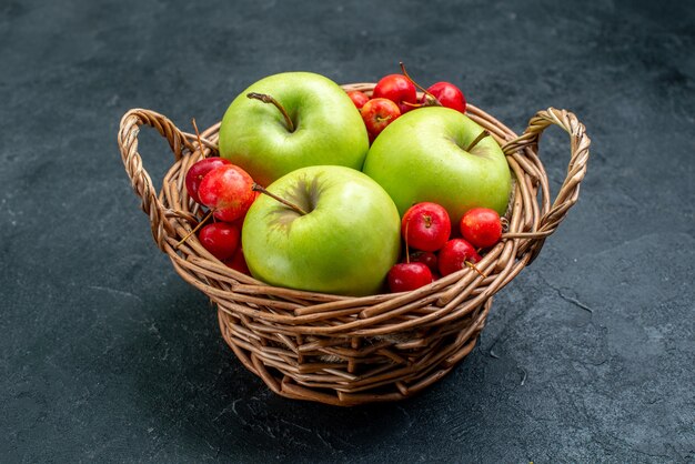 Vorderansichtkorb mit Fruchtäpfeln und Süßkirschen auf Frischbaum der Fruchtbeerenzusammensetzung der dunklen Oberfläche