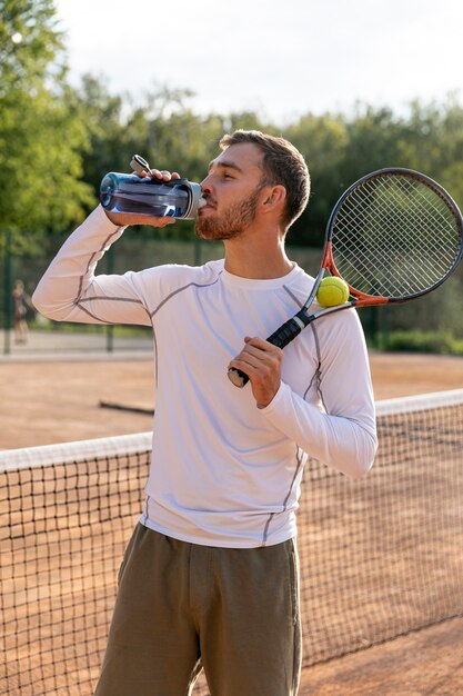 Vorderansichtmann, der auf Tennisplatz hydratisiert