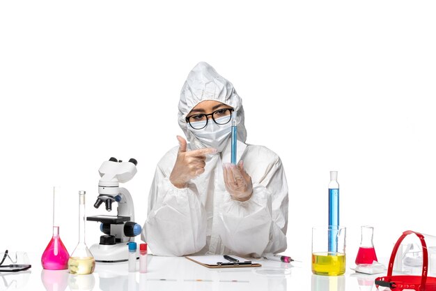 Vordere Ansicht junge Chemikerin im speziellen Schutzanzug mit Flasche mit blauer Lösung auf weißem Schreibtisch Covid-Chemie-Viruslabor