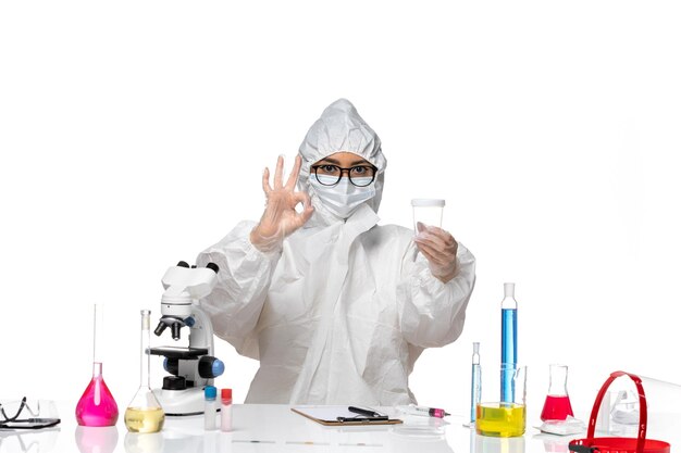 Vordere Ansicht junge Chemikerin in speziellem Schutzanzug mit leerem Kolben auf hellweißem Hintergrundlabor-Covid-Chemie-Virus