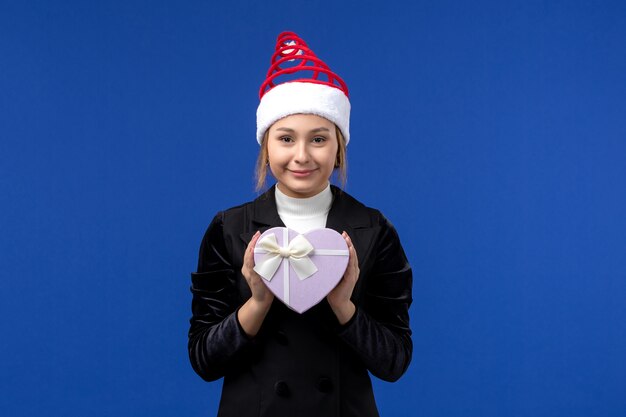 Vordere Ansicht junge Dame, die herzförmiges Geschenk auf Neujahrs-Emotionsfeiertag der blauen Wand hält